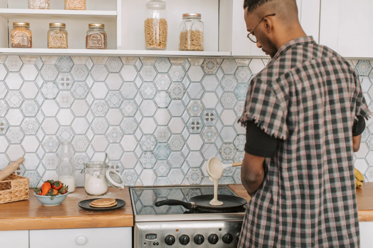 Hombre preparando tortitas en los fogones de una cocina con paredes de azulejos modernos
