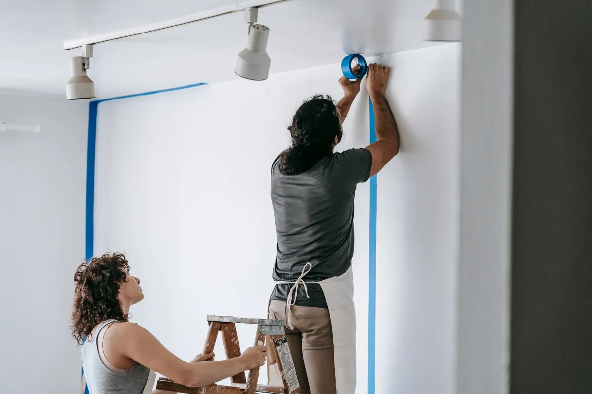 Hombre y mujer colocando juntos cinta de carrocero durante la reforma de una vivienda