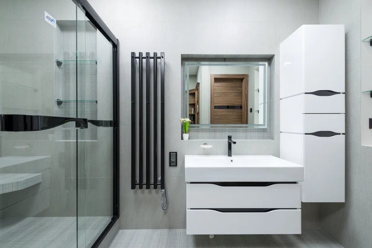 Lavabo blanco con mueble y espejo en un baño luminoso con mampara