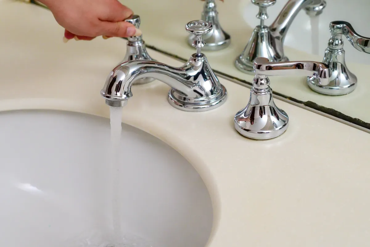 Mano abriendo un grifo cromado con el agua corriendo en un baño elegante
