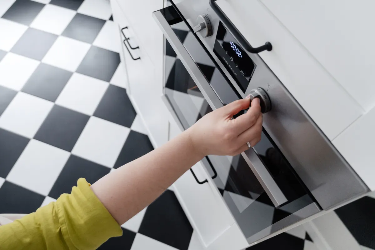 Mano ajustando el mando de temperatura de un horno moderno de acero inoxidable