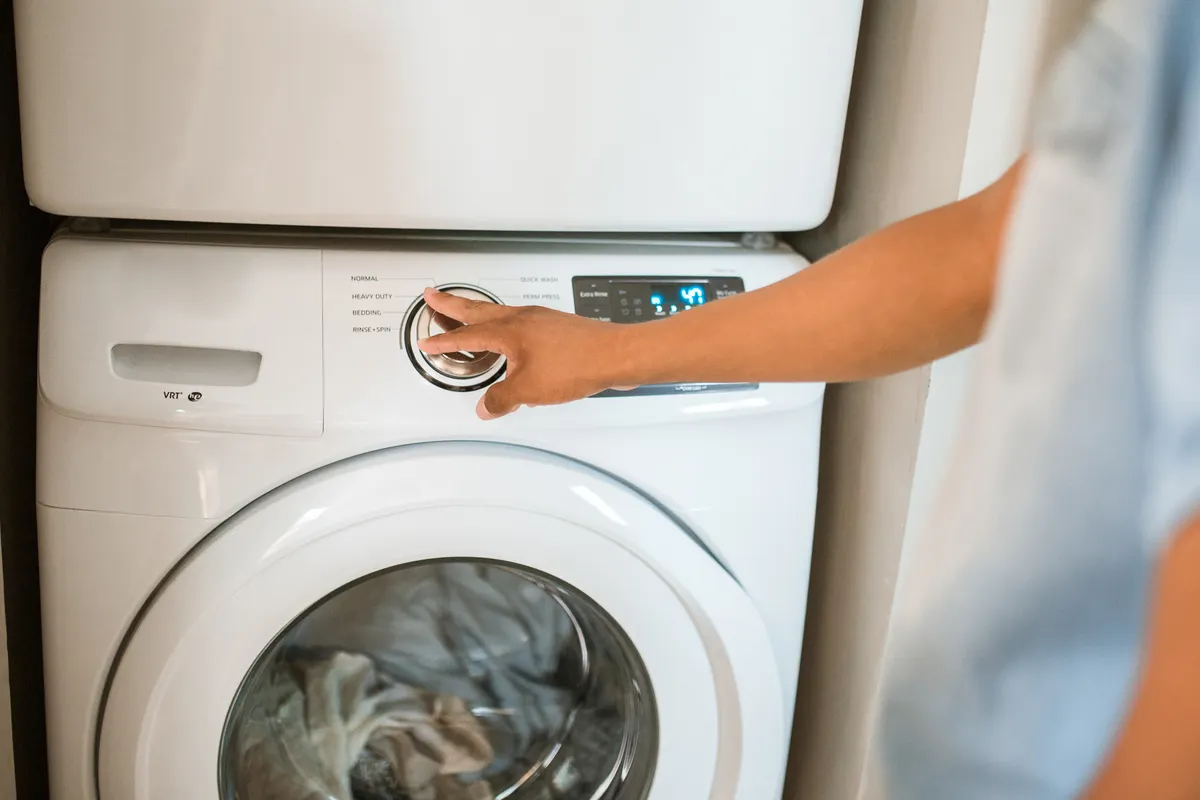 Mano girando el selector de programas de una lavadora de carga frontal con la ropa dentro