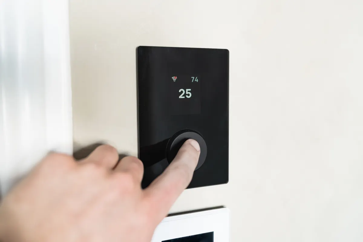 Mano regulando un termostato inteligente de pared