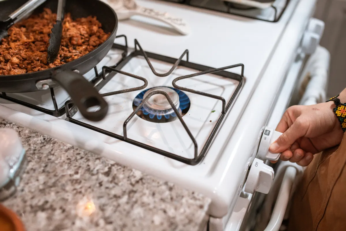 Mano regulando una cocina de gas con carne cocinándose en una sartén
