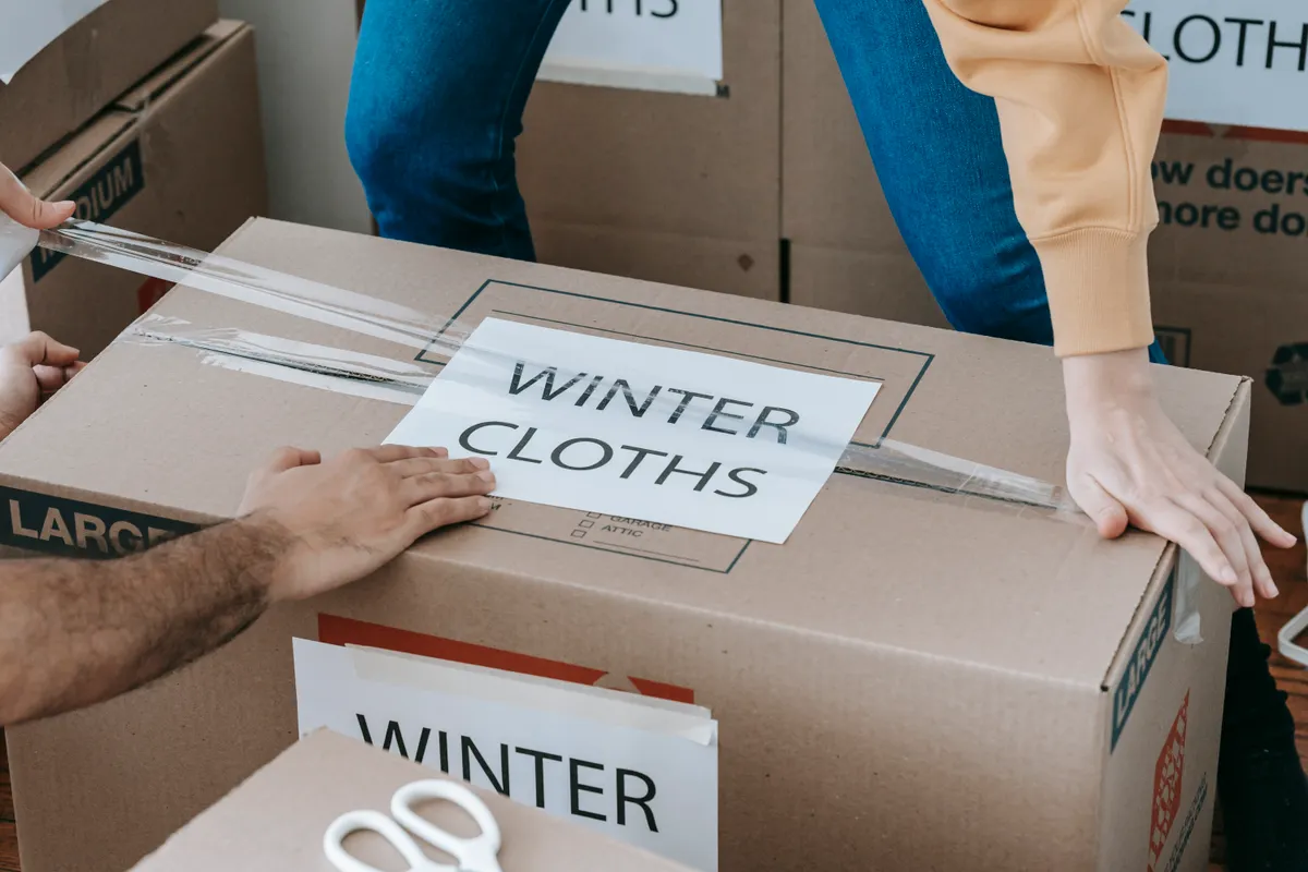 Manos embalando una caja rotulada para la ropa de invierno antes de una mudanza