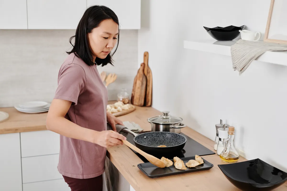 Mujer cocinando dumplings en una sartén en una cocina moderna
