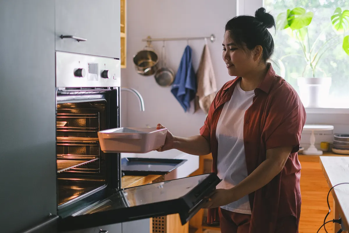 Mujer colocando una fuente en el horno en una cocina soleada