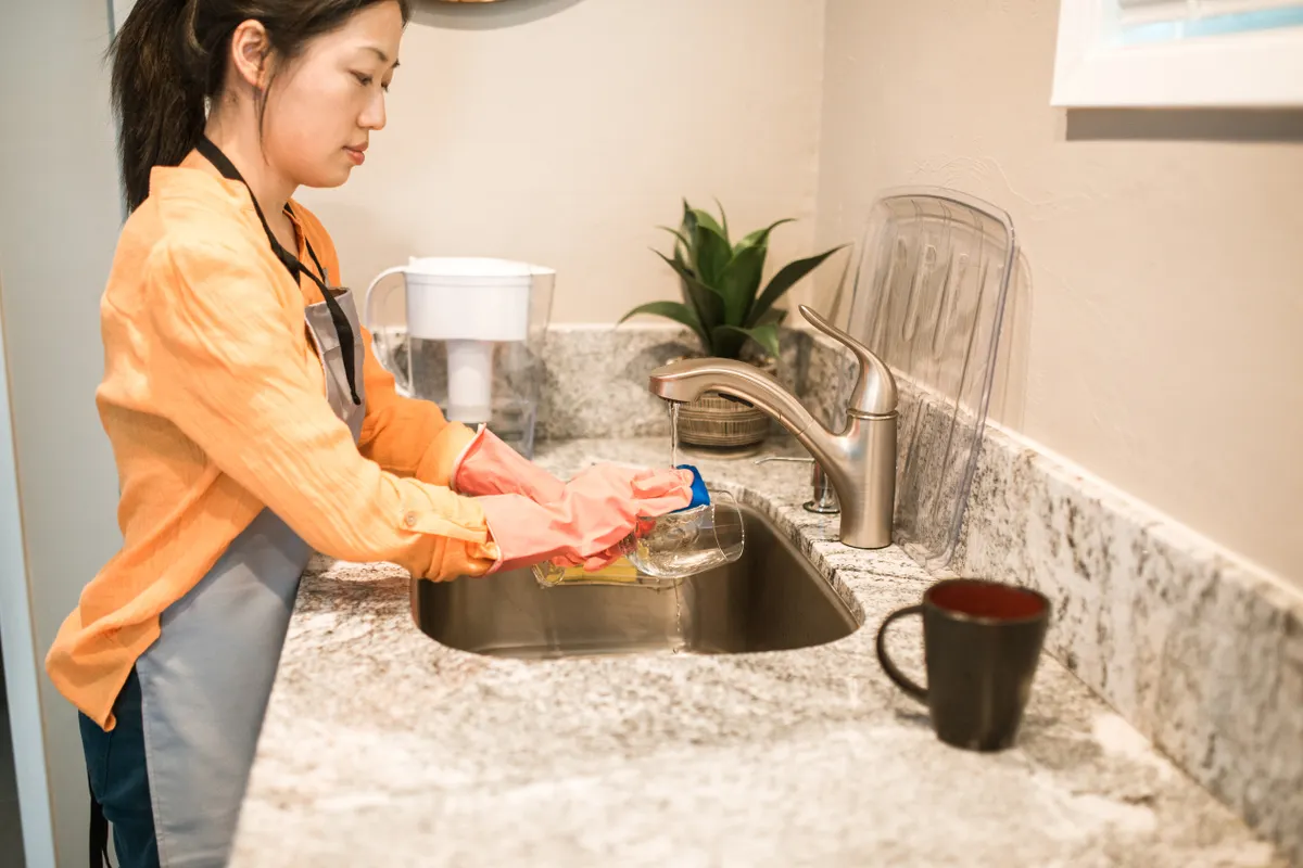 Mujer con guantes lavando un vaso en el fregadero de la cocina