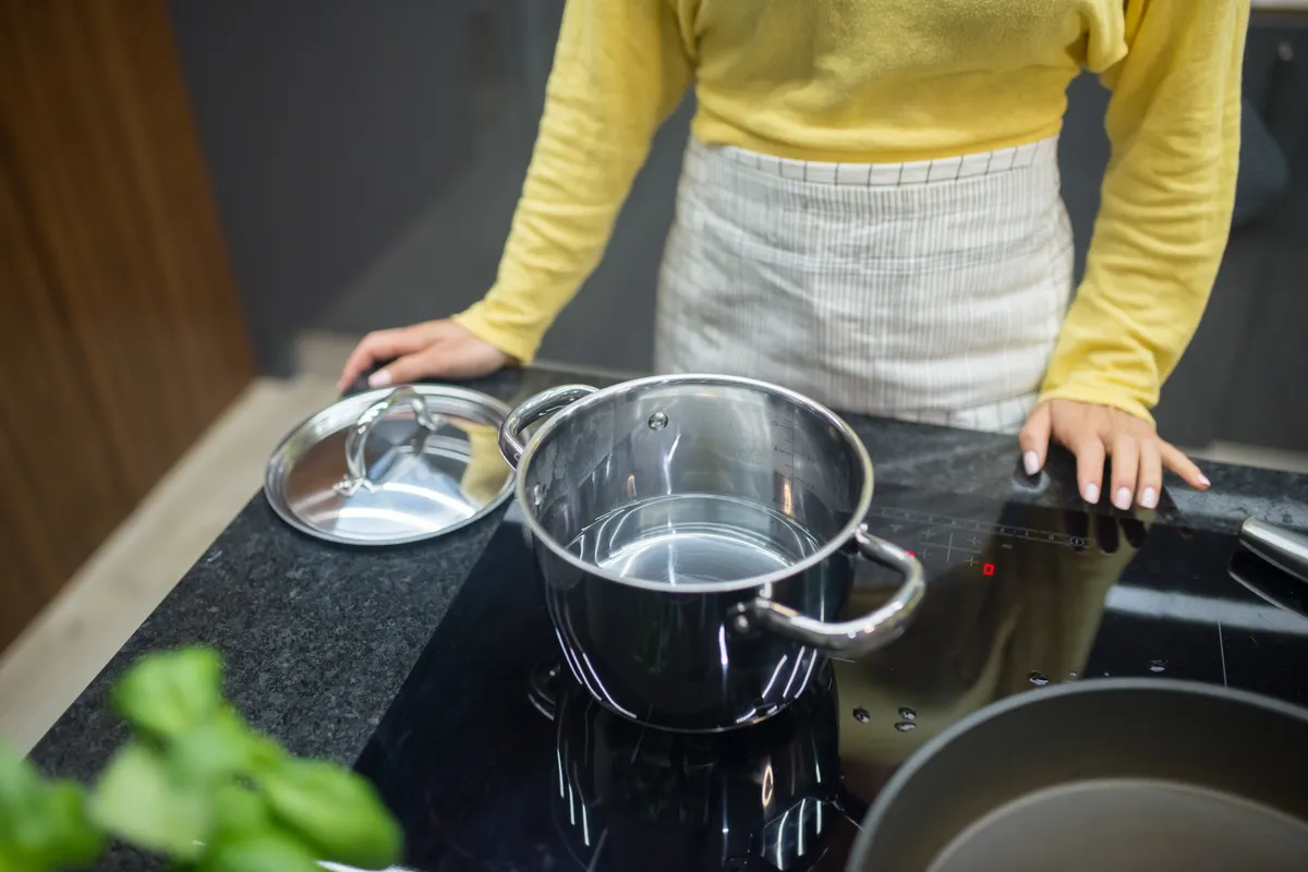 Mujer con jersey amarillo cocinando con una olla de acero inoxidable en una placa de inducción