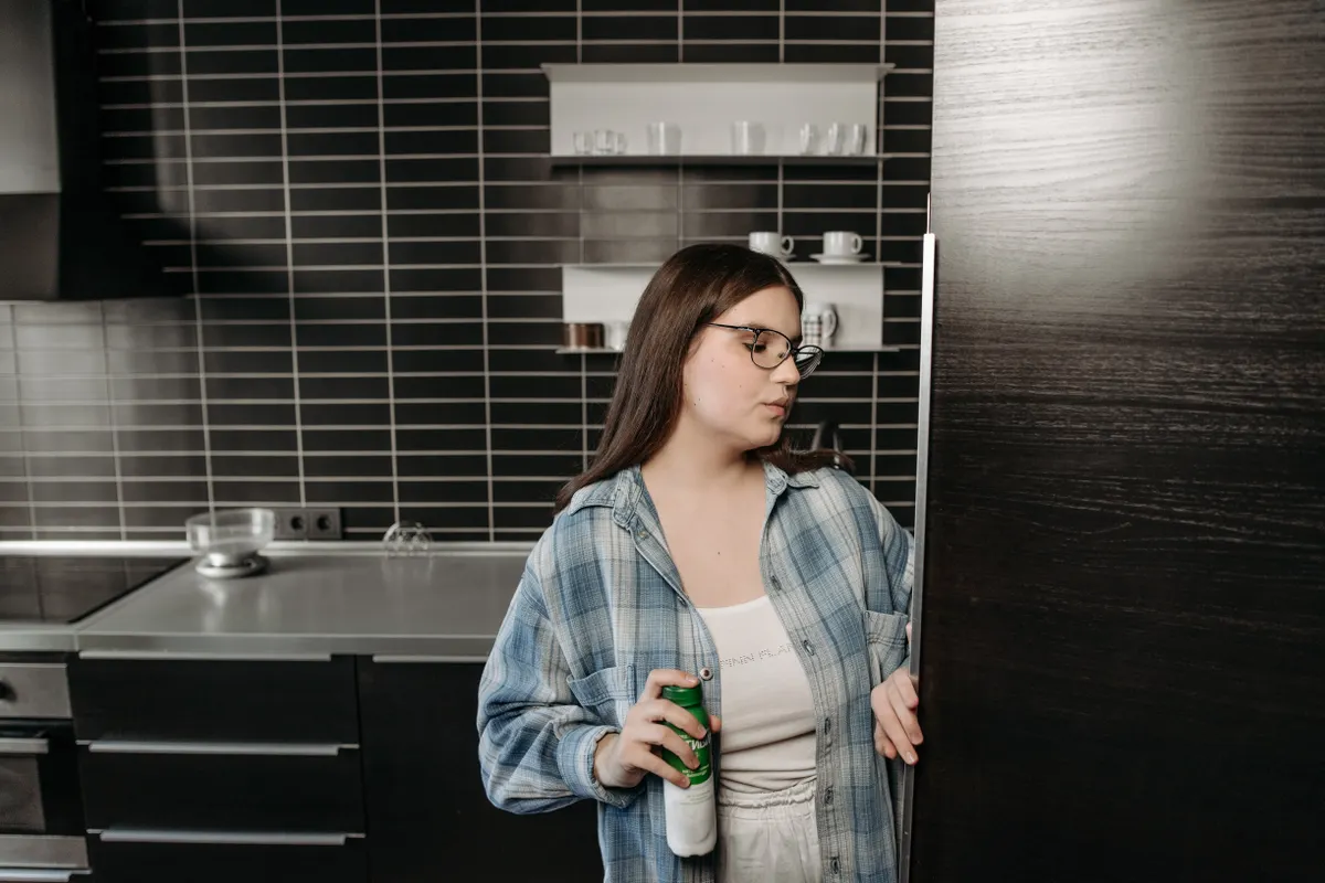 Mujer con una bebida en la mano abriendo el frigorífico de una cocina moderna