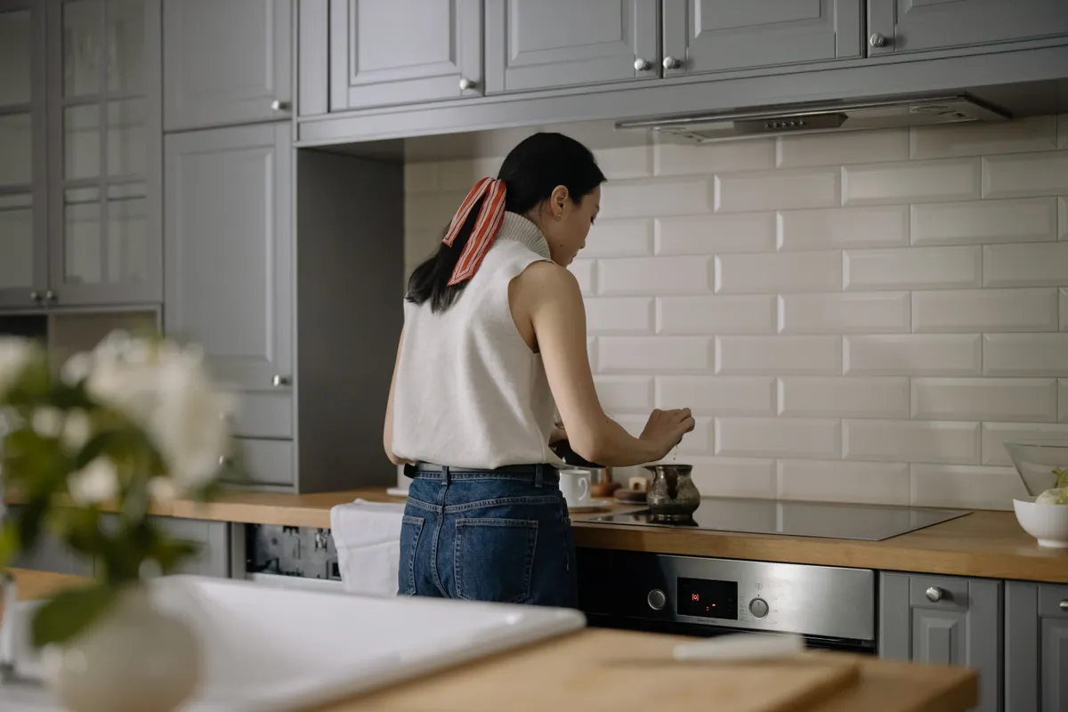 Mujer de espaldas cocinando frente a los fogones de una cocina moderna
