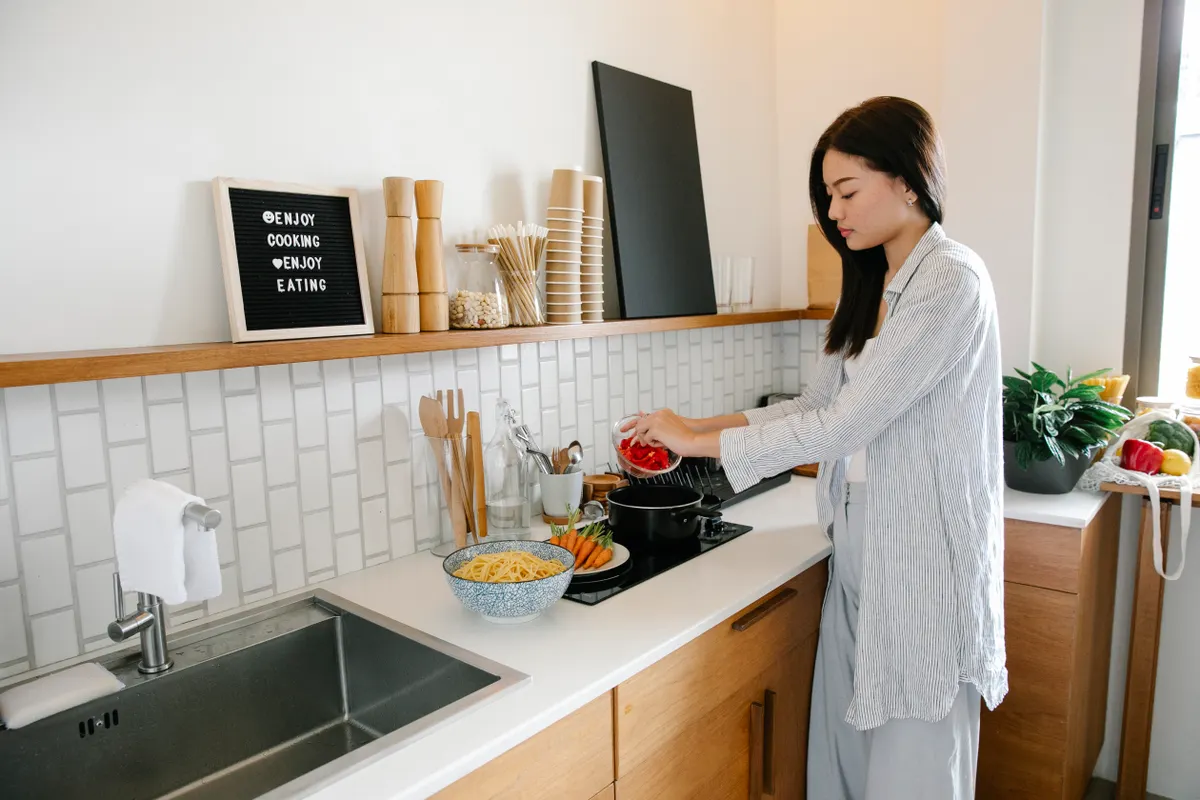 Mujer echando verduras troceadas en un cazo junto a los fogones mientras cocina pasta