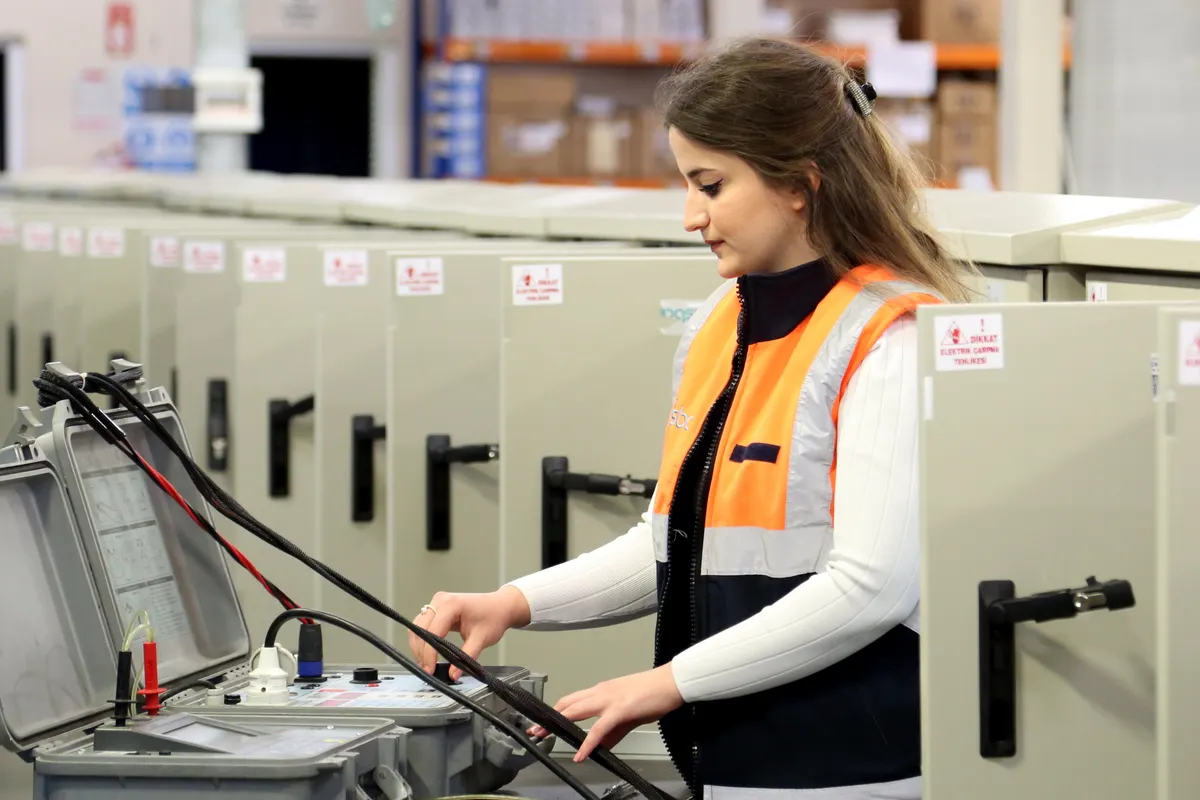 Mujer electricista con equipo de seguridad revisando cuadros eléctricos en interior
