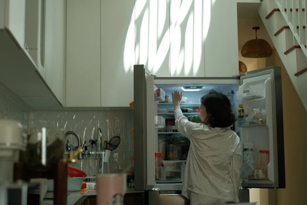 Mujer en pijama mirando el frigorífico en una cocina acogedora con luz cálida