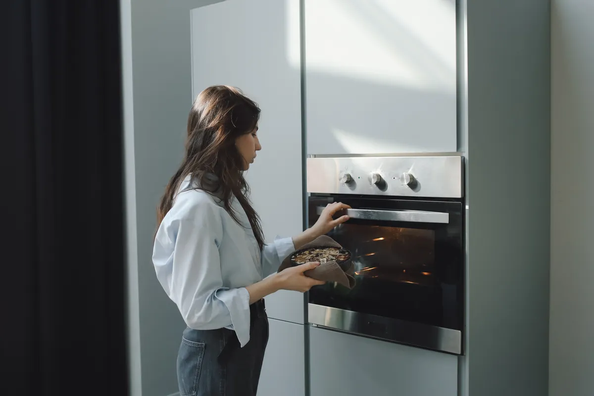 Mujer joven metiendo una fuente en el horno en una cocina moderna con luz natural