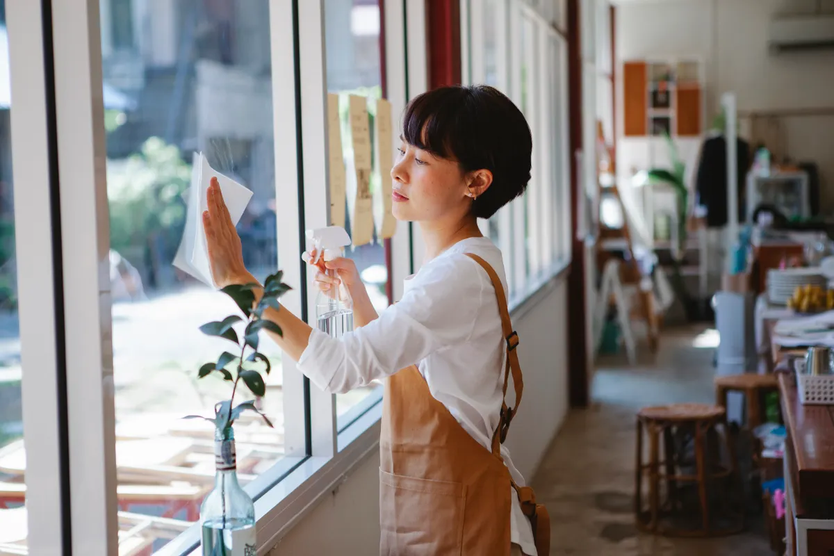 Mujer limpiando el cristal de un restaurante con un pulverizador y papel