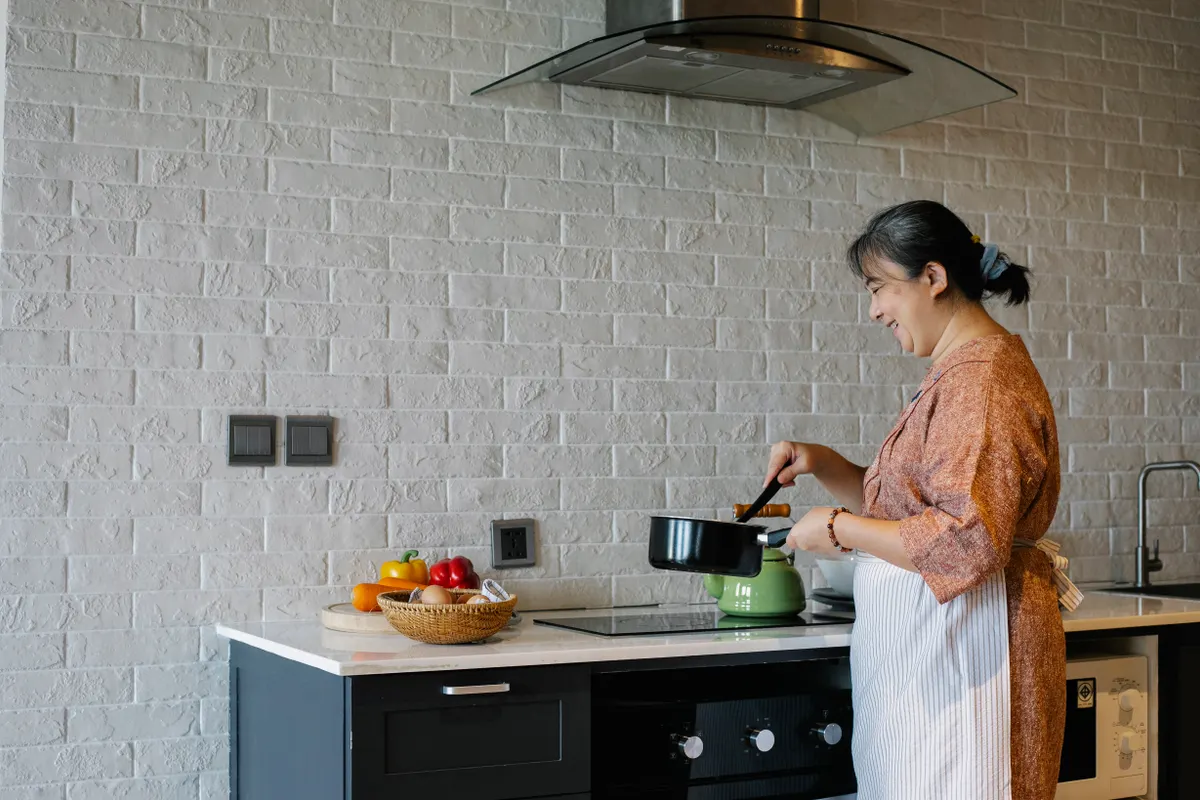 Mujer mayor con delantal sujetando una sartén junto a los fogones mientras prepara la comida