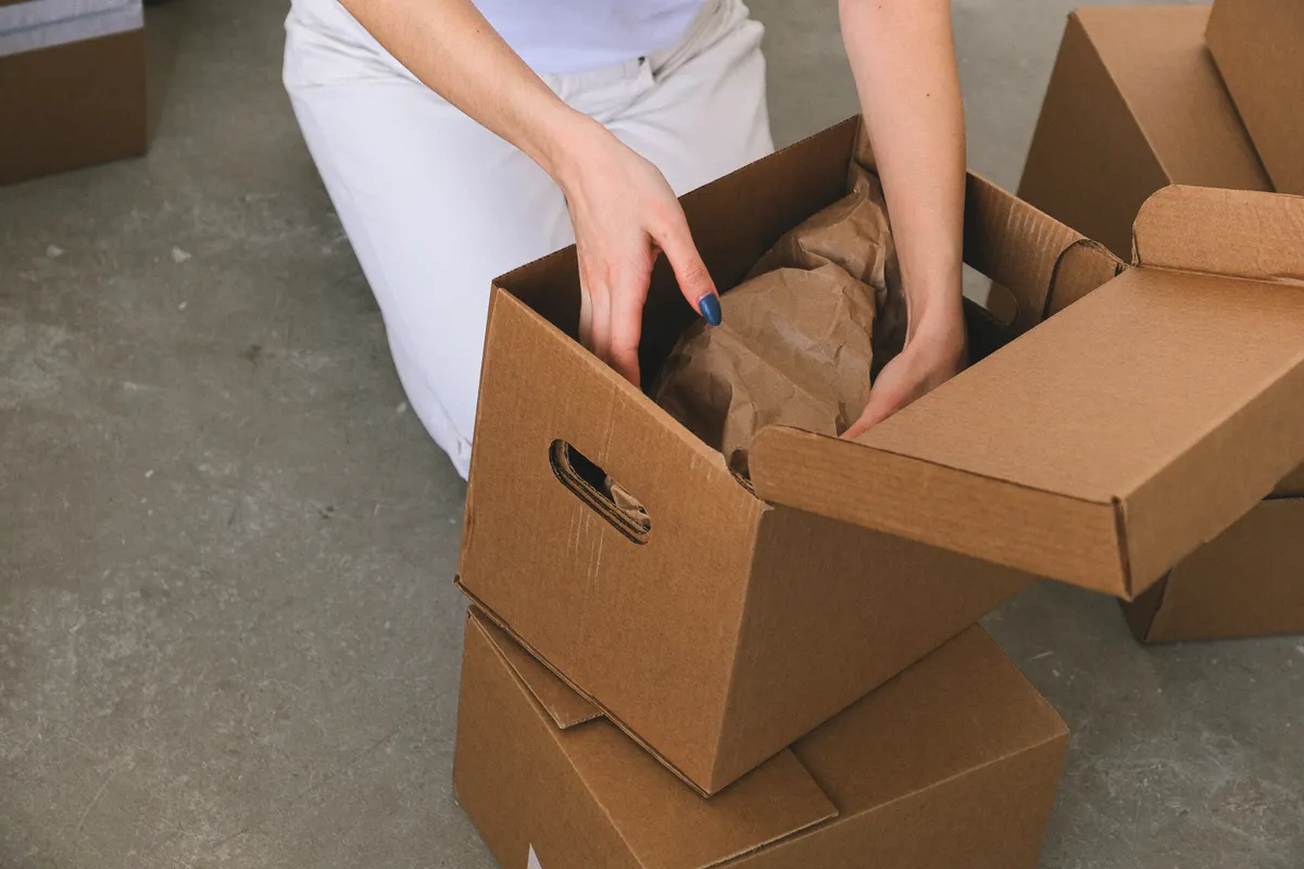Mujer metiendo objetos envueltos en una caja de cartón para su mudanza, vista desde arriba
