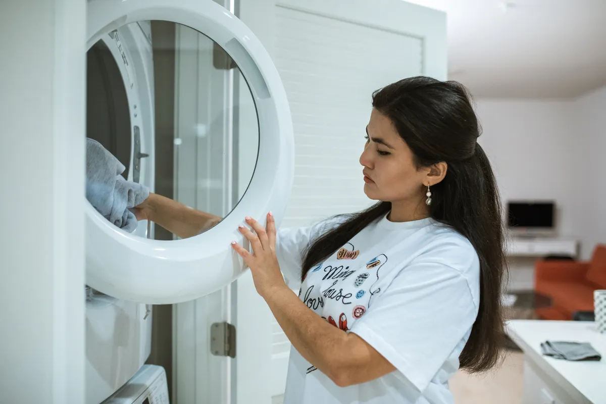 Mujer metiendo una sudadera gris en el tambor de una secadora instalada en columna, con la puerta abierta