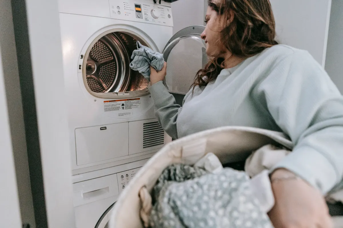 Mujer seria con ropa informal metiendo la colada en una lavadora moderna, vista de perfil