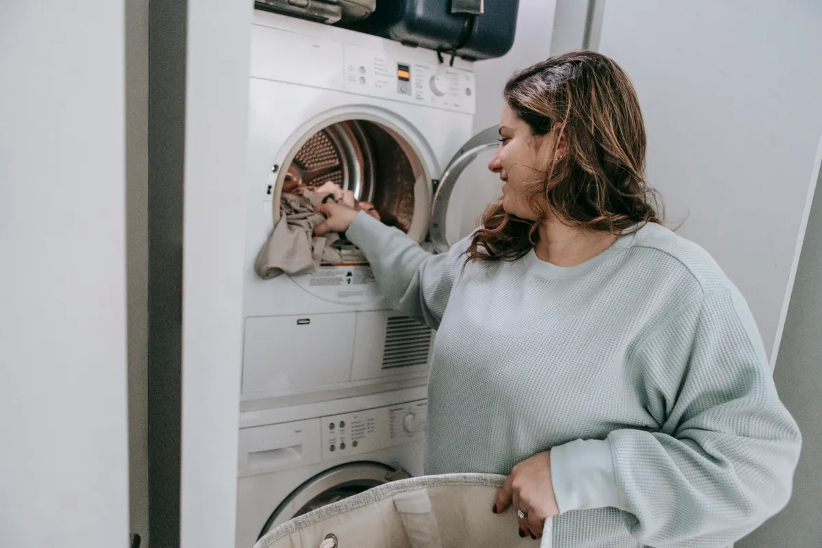 Mujer sonriente sentada en el baño metiendo ropa sucia en una lavadora blanca moderna