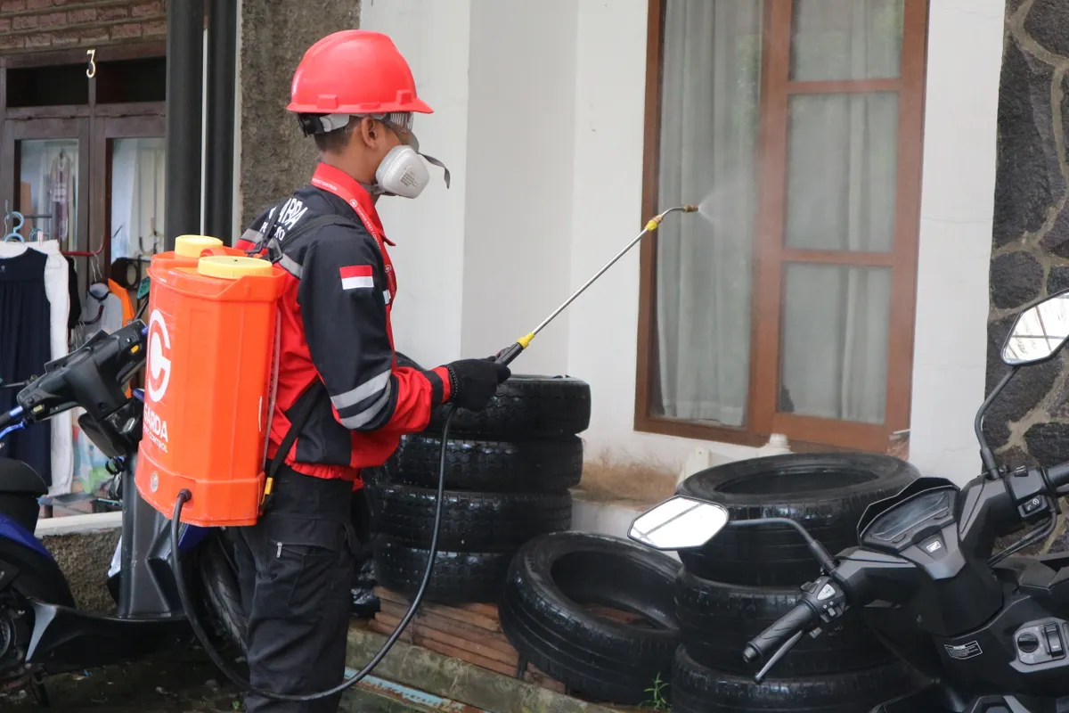 Operario con equipo de seguridad pulverizando desinfectante en el exterior de un edificio