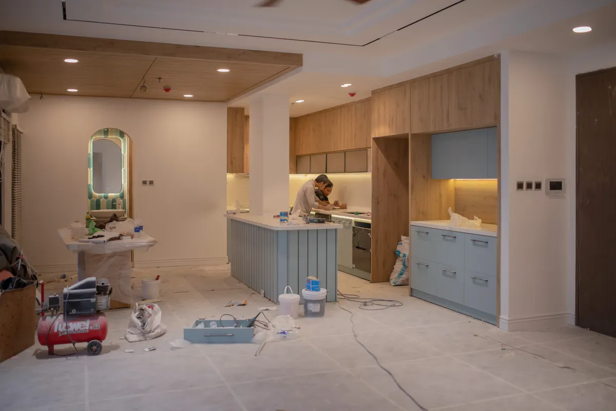 Operarios montando los muebles de una cocina en plena reforma, con el suelo protegido, cubos y herramientas