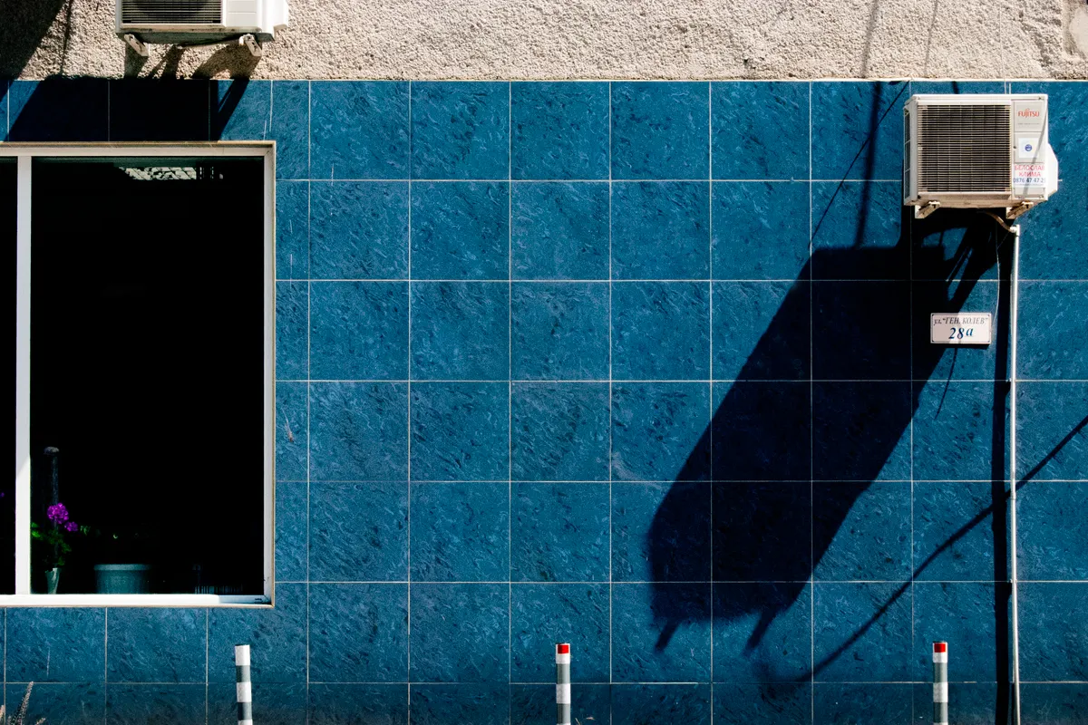 Pared urbana de azulejos azules con un aire acondicionado y un marcado juego de sombras