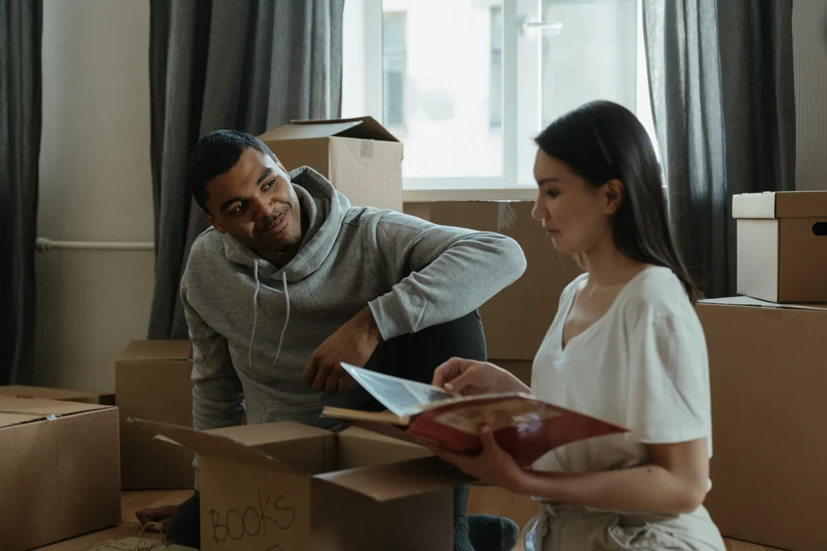 Pareja desembalando cajas en su nueva casa mientras mira un álbum de fotos