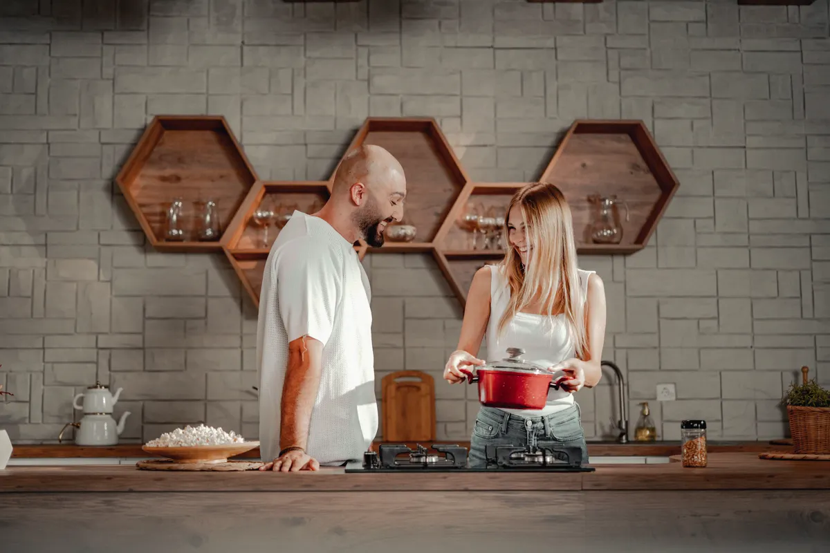 Pareja feliz cocinando en equipo en una cocina con estantes hexagonales
