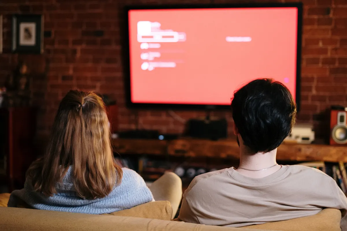 Pareja viendo la televisión en el sofá de un acogedor salón con paredes de ladrillo