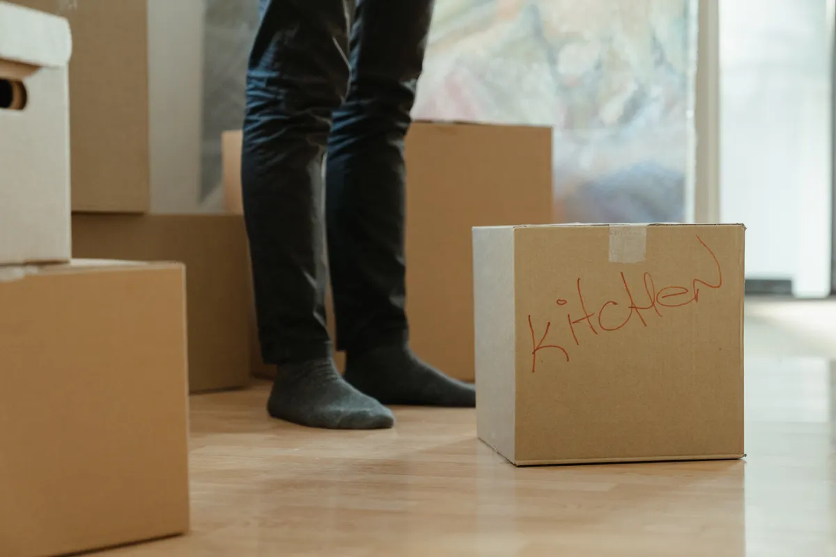 Persona de pie en una habitación rodeada de cajas de mudanza rotuladas para la cocina