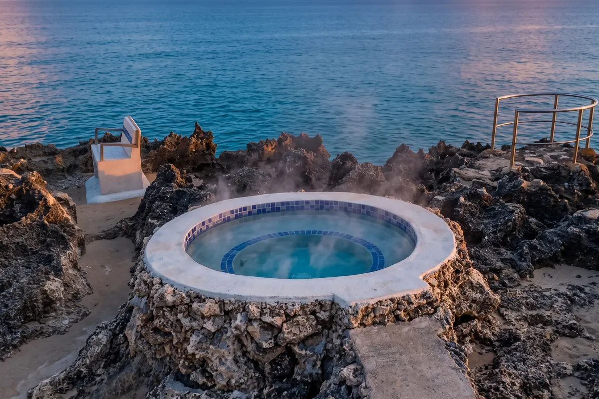 Poza natural de agua caliente entre rocas junto al mar, con vapor al atardecer