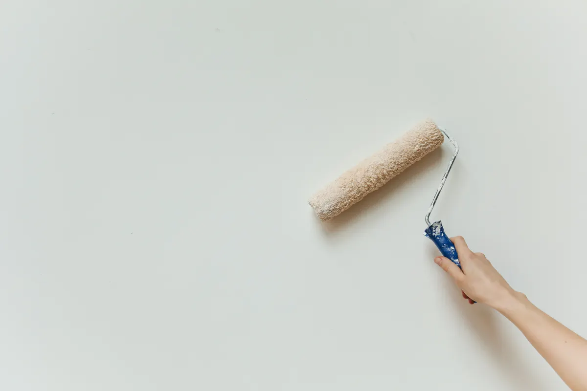 Primer plano de una mano aplicando pintura con rodillo sobre una pared en obras