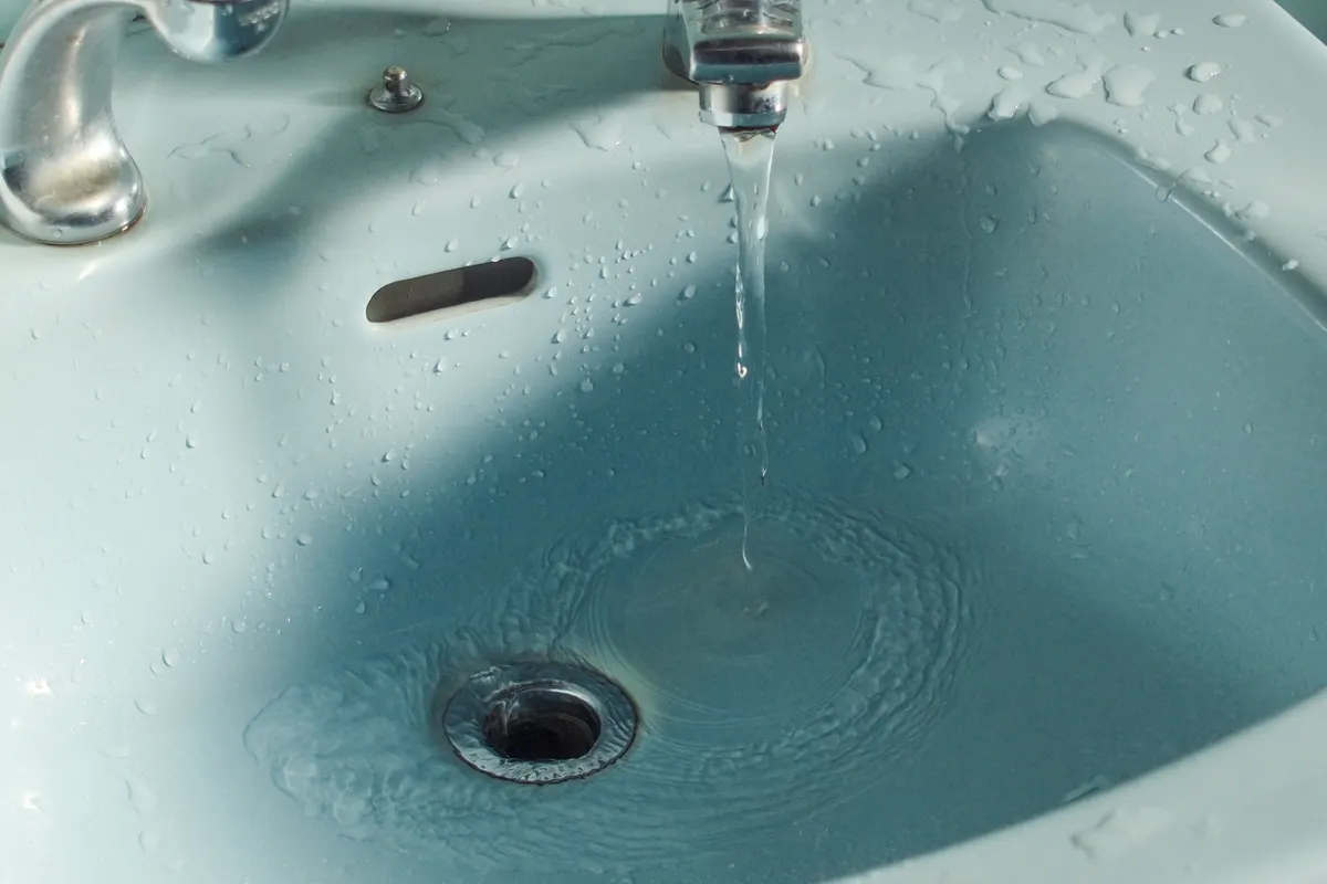 Primer plano del agua cayendo de un grifo en el lavabo del baño
