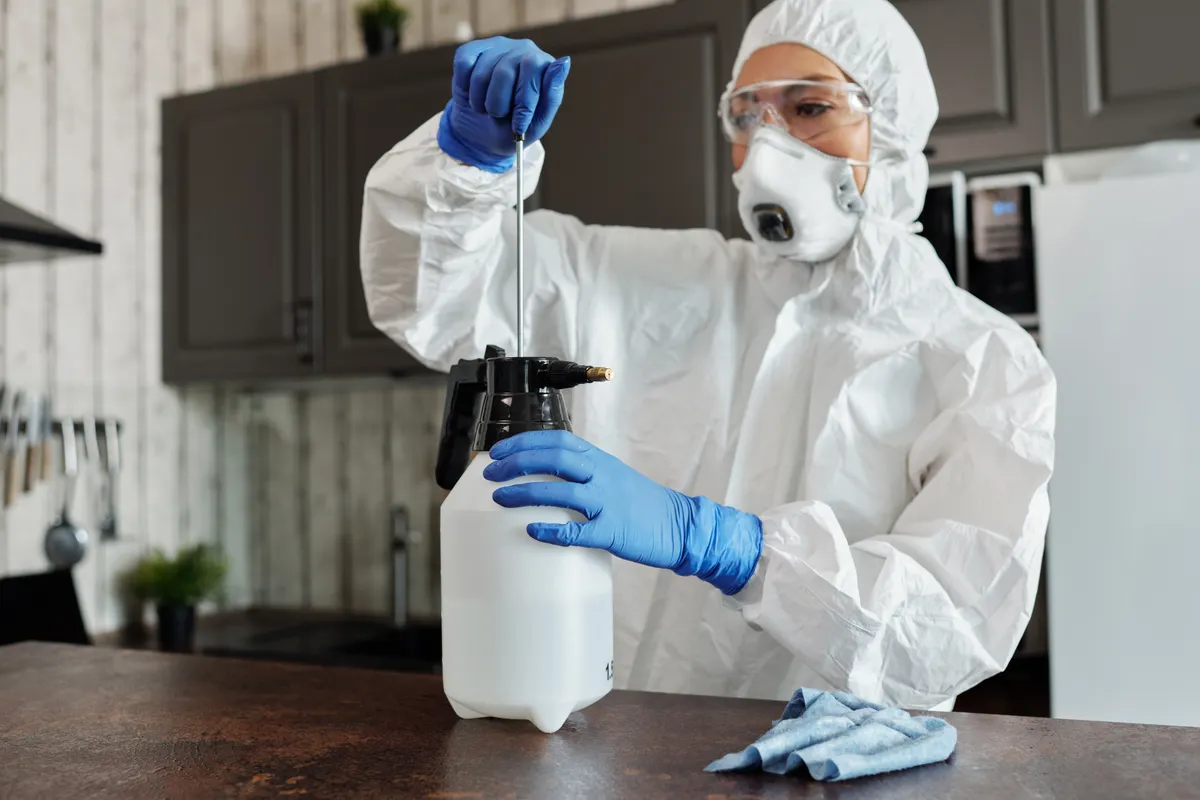 Profesional con mono, gafas y mascarilla preparando un pulverizador de presión en la encimera de una cocina