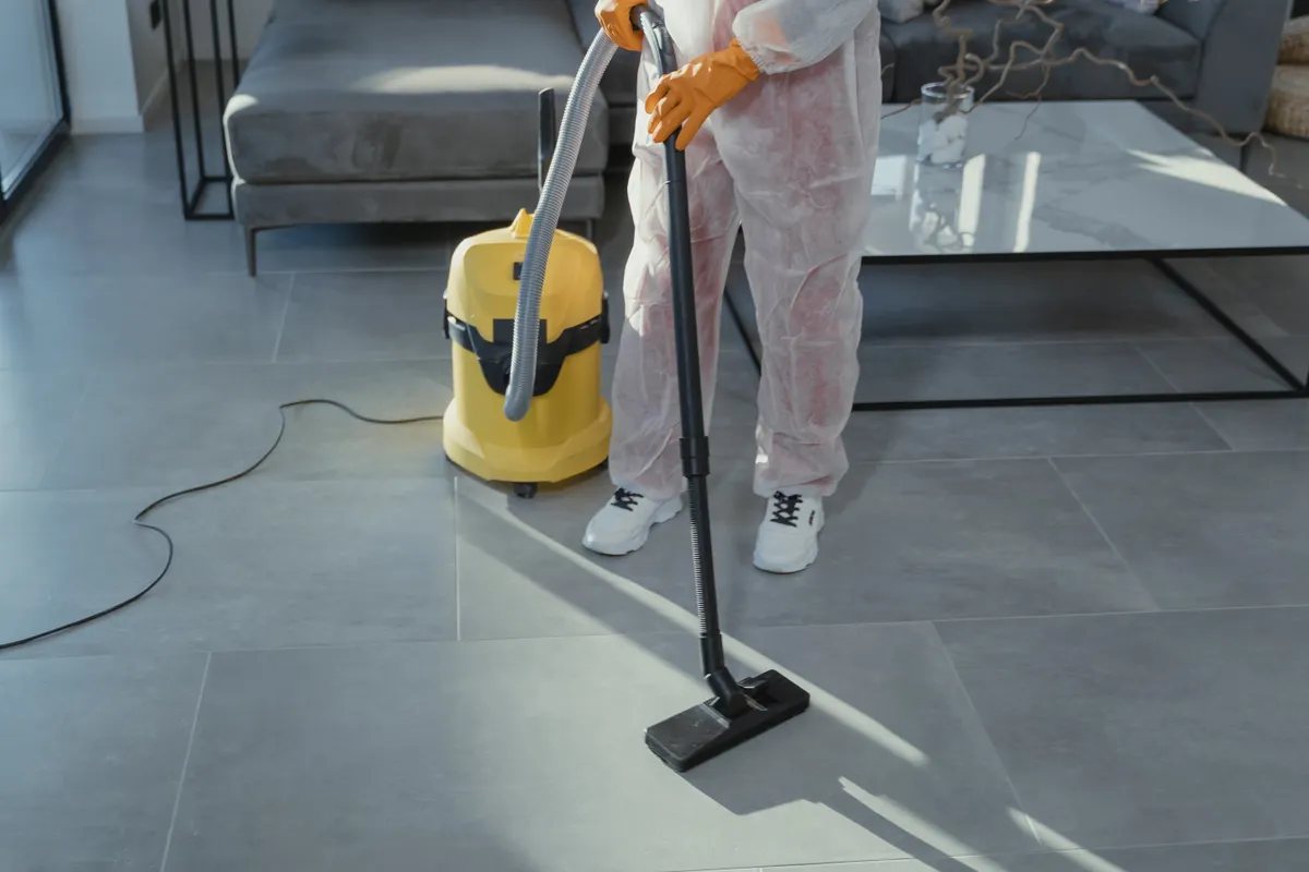 Profesional de la limpieza con equipo de protección aspirando el suelo de un salón moderno