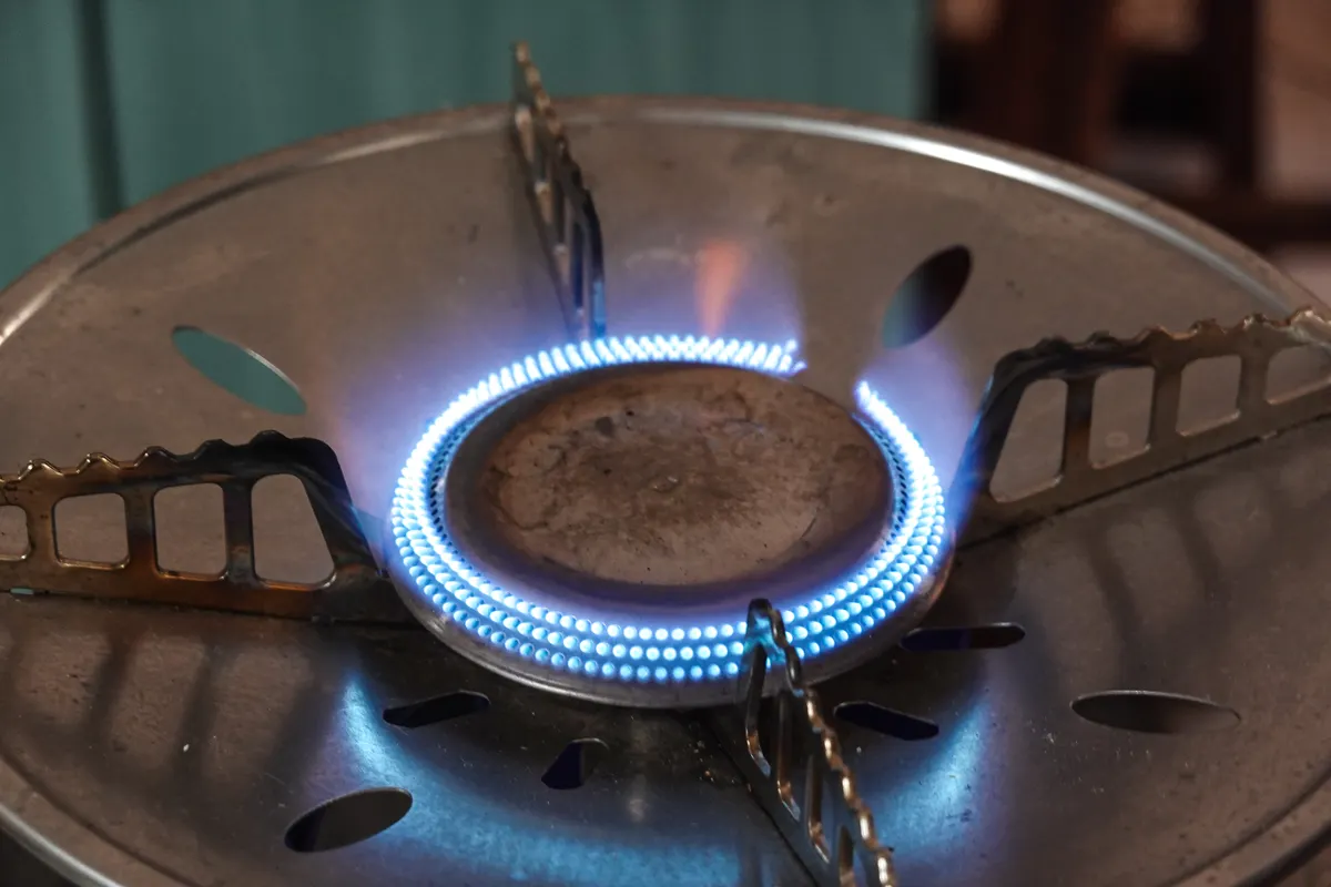 Quemador de una cocina de gas encendido, con llamas azules y la rejilla metálica