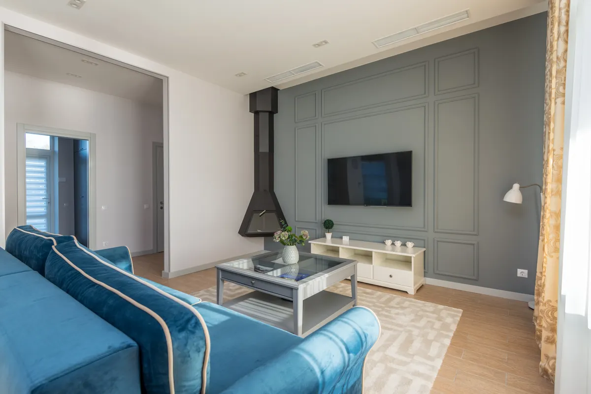 Salón con sofá azul, televisor colgado en la pared y decoración elegante