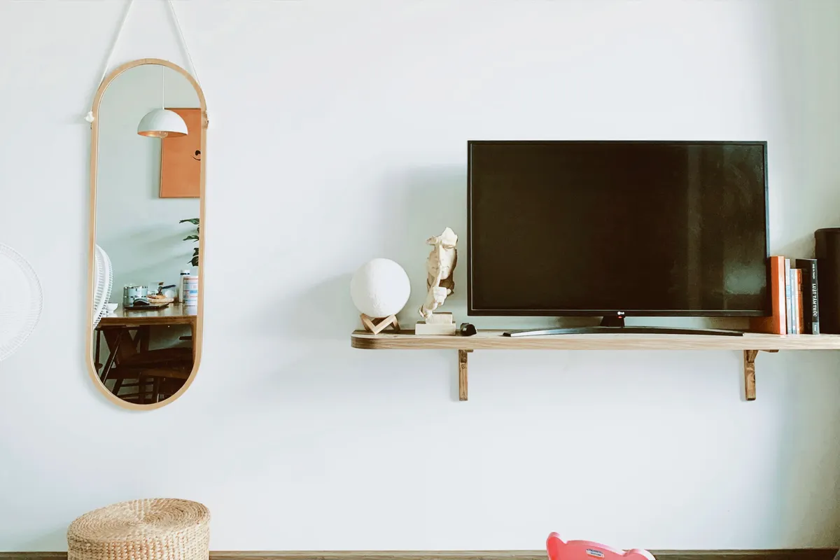 Salón con televisor de pared, un espejo y decoración moderna sobre una pared blanca