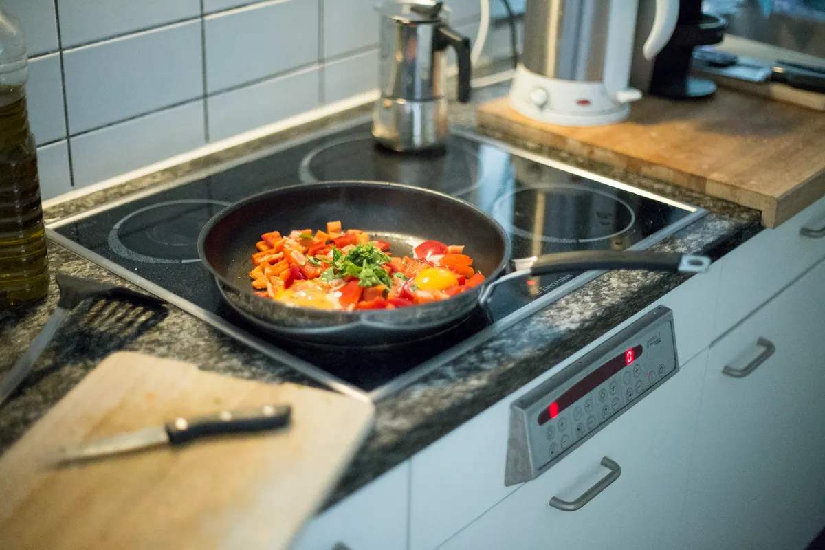 Sartén de colores con huevos y verduras en una placa eléctrica de una cocina moderna