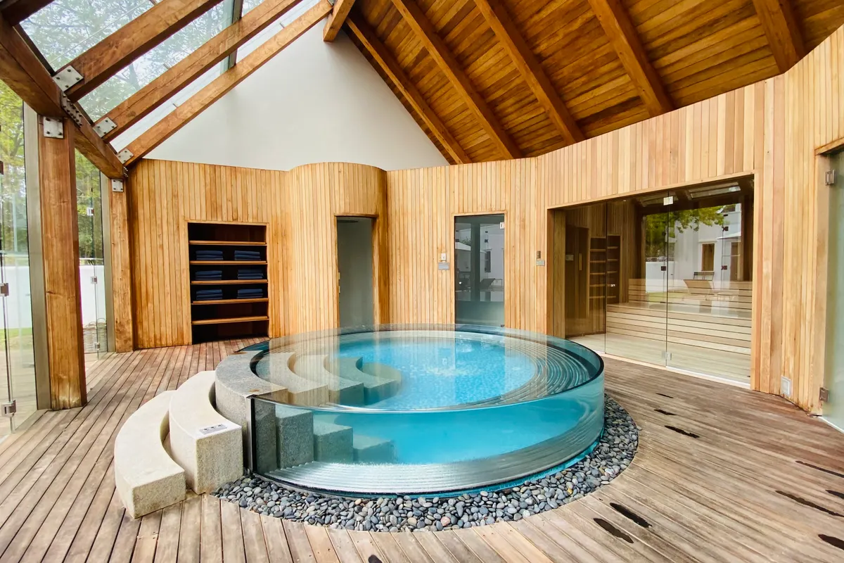 Spa circular de paredes de cristal con agua limpia y transparente en una sala de bienestar revestida de madera
