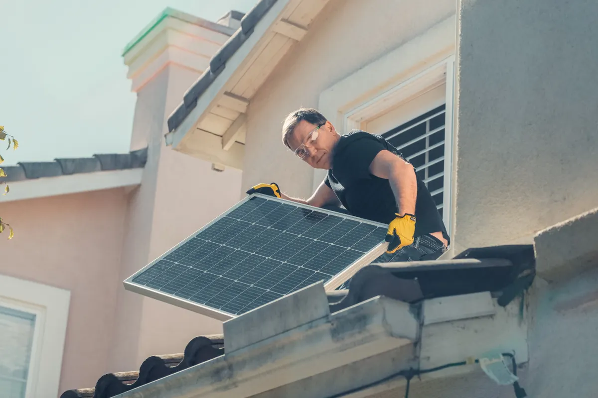 Técnico con equipo de protección instalando placas solares en el tejado de una casa