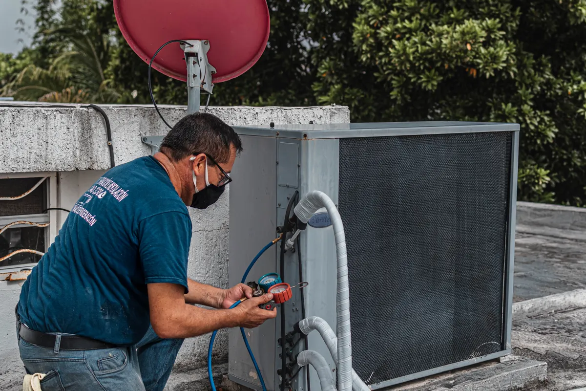 Técnico con mascarilla reparando un aparato de aire acondicionado con un juego de manómetros