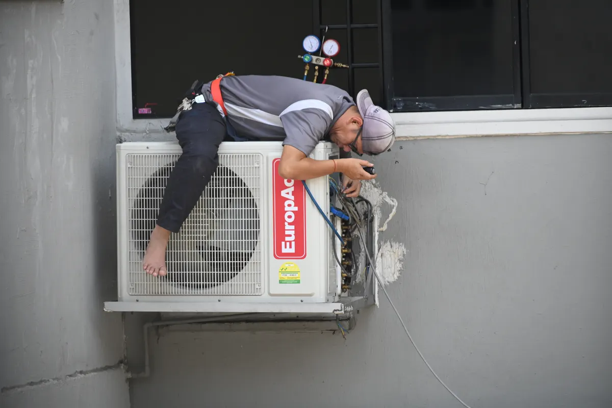 Técnico reparando la unidad exterior de un aire acondicionado instalada en la fachada de un edificio