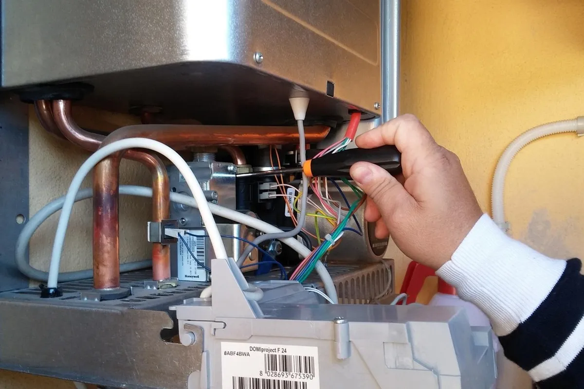 Técnico revisando con un destornillador el cableado y las tuberías de cobre de un calentador abierto
