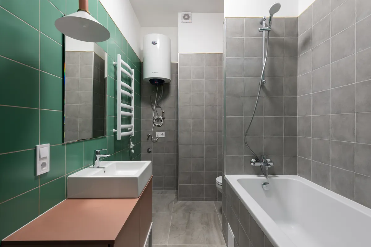 Termo eléctrico blanco instalado en lo alto de la pared de un baño alicatado en gris y verde