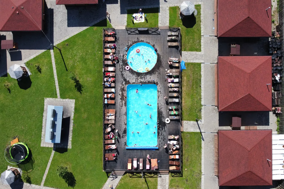 Vista desde un dron de las piscinas de un complejo con bañistas y edificios de tejado rojo